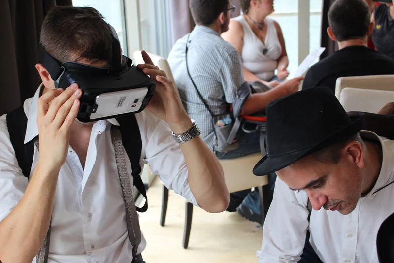 Un participant en chemise blanche ajuste son casque VR pendant l'épreuve, un coéquipier à côté.