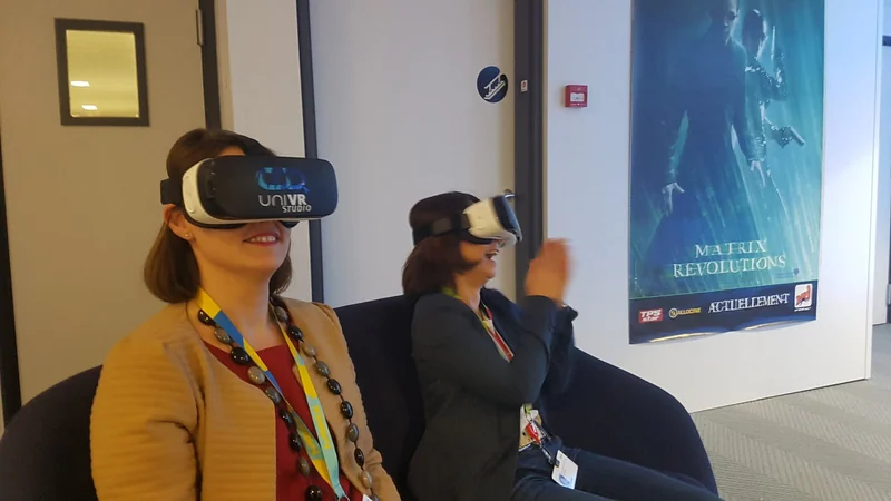 Une participante sourit sous son casque VR, une autre découvre l'expérience à l'arrière-plan.