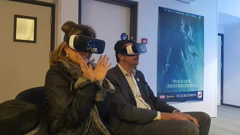 Deux participants sous casque VR, assis devant une affiche du film Matrix Revolutions.