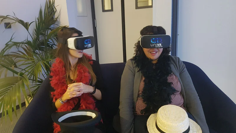 Deux participantes déguisées, boa de plumes et canotier posé à côté, sous casque VR.