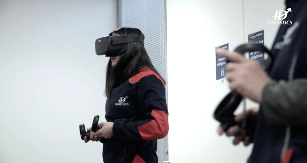 Une opératrice ID Logistics manipule les manettes sous casque VR, une collègue à côté d'elle.